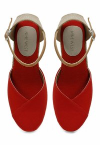 Scarpe espadrillas in tela rossa con punta chiusa e design anteriore intrecciato. Presentano una cinghia alla caviglia color beige e un accento in fibra naturale testurizzata.