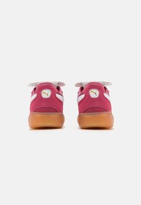 Sneakers Puma con una parte esterna in suede rosa, dettagli bianchi e una suola in gomma beige. Presentano un'etichetta con logo e una linguetta imbottita per il comfort.