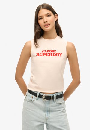 Top sans manches rose clair avec "J'ADORE SUPERDRY" en lettres rouges grasses. Associé à un jean bleu clair taille haute et une ceinture noire avec une boucle en argent.