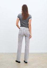 Siva majica kratkih rukava s bijelim rubom, uparena s svijetlosivim trapericama viskog struka. Ravnog kroja s dva stražnja džepa i suptilnom teksturom.