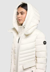 Gewatteerde witte jas met een grote capuchon, voorzien van een ritssluiting aan de voorkant, zijzakken en een zwart logo-opdruk op de linker mouw.