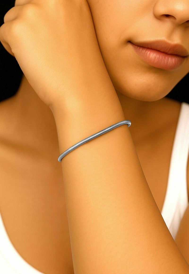 Blå metall armbånd på et lys brun håndledd, glatt tekstur, sylindrisk form, båret rett over håndleddsbeinet.