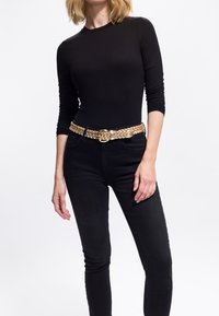 Sort langærmet top parret med højtaljede sorte jeans. Et fletbælte i guld fremhæver taljen. Glat stoftekstur hele vejen igennem.