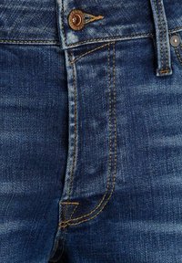 Mörkblå denimjeans med en klassisk femfickedesign, kopparbeslag och gula sömmar längs sömmarna och fickorna.