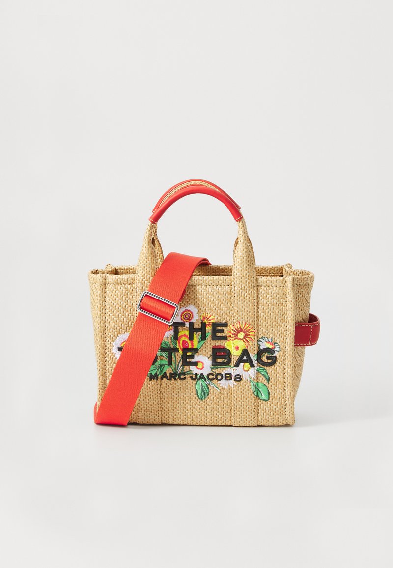 Small woven tote bag with red top handles and strap, embroidered with colorful flowers and black text "THE TOTE BAG MARC JACOBS."