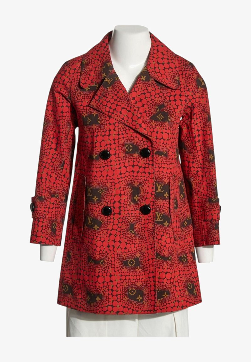 Manteau rouge croisé avec boutons noirs, présentant un motif de cercles rouges et de logos monogrammes marron, exposé sur un mannequin blanc.