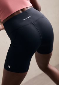 Pantaloni corti neri a vita alta con una vestibilità aderente, dotati di un logo sulla cintura e tessuto liscio e elastico per comfort e flessibilità.