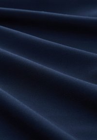 Tela azul marino con una textura suave, que presenta pliegues diagonales que crean profundidad y dimensión en la caída.