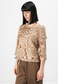Beige bestickte Bluse mit filigranen Blattmustern und strukturierten Akzenten. Dreiviertelärmel und runder Ausschnitt.