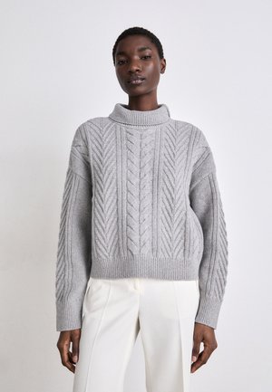 Gray knitted sweater with a high turtleneck, featuring a cable pattern and ribbed hem. Paired with white tailored pants.