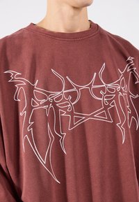 Camiseta de algodón granate con un atrevido gráfico abstracto blanco en la parte delantera, cuello redondo y corte relajado con textura suave.