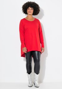 Rote Tunika mit langen Ärmeln und abgerundetem Saum, kombiniert mit schwarzen Leggings und silbernen Cowboystiefeln, im lässigen Schnitt und mit weichem Stoff.
