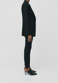 Musta räätälöity bleiseri, jossa on löysä istuvuus, yhdistettynä slim fit -mustiin housuihin ja tyylikkäisiin avokasneuloihin. Liukas pinta, minimalistinen muotoilu.