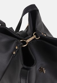 Schwarze strukturierte Lederhandtasche mit goldfarbigem Verschluss und Ringbeschlägen, Fokus auf die offene Oberseite und detaillierte Nähte vor weißem Hintergrund.