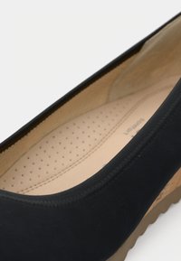 Gros plan sur une chaussure noire sans lacets avec une semelle intérieure beige coussinée et perforée et une semelle extérieure marron texturée.