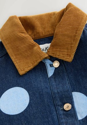 Jachetă din denim albastru închis cu buline mari albastre deschise, guler din catifea maro și nasturi metalici cu capse.