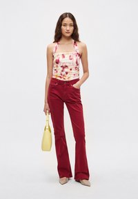 Kukallinen haltertoppi rypytyksellä, yhdistetty korkeavyötäröisiin punaisiin liehuviin housuihin. Asusteina keltainen käsilaukku ja teräväkärkiset beiget kengät.