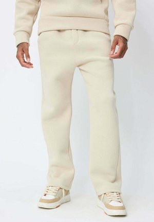 Jogging en molleton beige avec une coupe décontractée, dotés d'une taille élastique avec cordon de serrage et de poches latérales, associés à des baskets crème et tan.