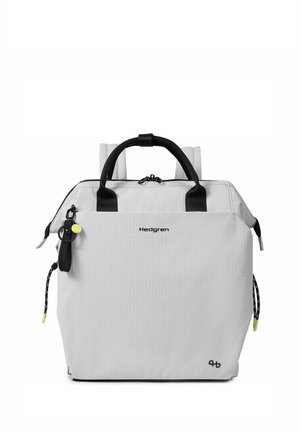 White Hedgren backpack with black handles, adjustable straps, zipper closures, and a small attached black and yellow keychain accessory.