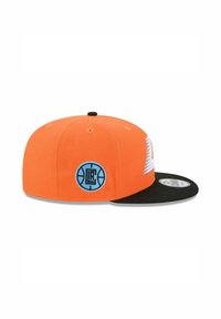 Oranger Cap mit schwarzem Schirm, ausgestattet mit einem blauen Basketball-Logo-Patch und einem Zickzack-Design an der Seite. Hergestellt aus Stoff mit strukturierter Form.