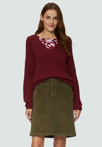 Bordeaux gebreide trui met een v-hals ontwerp en een wit bloempatroon bij de kraag, gecombineerd met een olijfgroene corduroy rok.