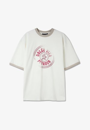 Bijela pamučna majica s oversized krojem, okruglim kremastim ovratnikom i ružičastim kružnim grafičkim otiskom koji glasi "DOLCE VITA PEGADOR."