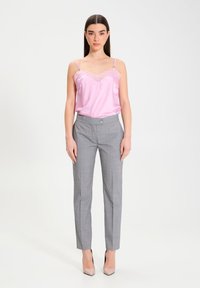 Camisola in raso rosa con bordi in pizzo, abbinata a pantaloni dallo stile sartoriale a quadri grigi. I pantaloni presentano una vita con un bottone. Tacchi alti in colori neutri.