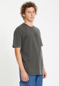 T-shirt di cotone grigio scuro con colletto rotondo e maniche corte, caratterizzato da un logo circolare sul petto e una vestibilità comoda.