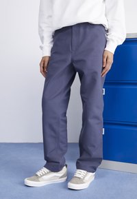 Pantalones de algodón azul con corte recto y detalles de costura visibles, combinados con zapatillas grises y blancas de textura de ante.