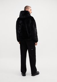 Black faux fur hoodie with a large hood, loose fit, and textured surface; paired with black cargo pants featuring side pockets.