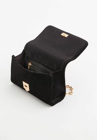 Sort ruskinds håndtaske med en guldfarvet lås og kæde. Den åbne låg afslører en lynlåslomme og et indre rum. Firkantet design.