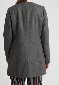 Abrigo de lana gris con corte recto, con cuello alto, mangas largas y detalles de costuras en la parte posterior.