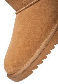 Brun ruskindsstøvle med syet kant på overdelen og tekstureret gummisål med et takket grebsmønster.