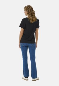 Čierne bavlnené tričko s krátkymi rukávmi, v kombinácii s modrými rozšírenými džínami, zobrazené zozadu, s vystaveným zakriveným šitím na vreckách.