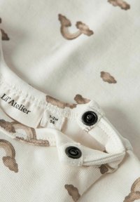 Body de bebé de algodón crema con un patrón de nubes marrones, que presenta un escote redondo y cierres de presión negros para una fácil vestimenta.