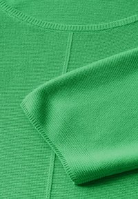 Vêtement en tricot vert avec un motif texturé, un col rond et des poignets côtelés, mettant en valeur un matériau doux et lisse.