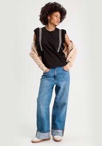 Top noir sans manches avec des détails en frange et des accents blancs, associé à un jean large bleu clair et des baskets blanches avec une semelle beige.