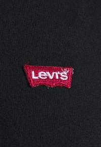Étiquette en tissu rouge Levi's avec texte blanc brodé sur fond de tissu noir texturé.