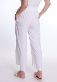 Witte wijde broek van lichtgewicht stof met een elastische tailleband en zijzakken. Draag met neutrale platte sandalen.