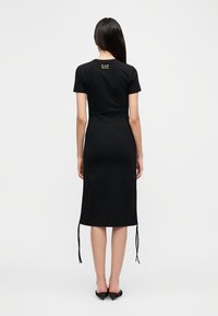 Μαύρο midi φόρεμα με κοντά μανίκια, με ίσια κοπή, πλαϊνούς δεσίματα στο τελείωμα και μικρό λογότυπο στην πλάτη. Λείο, ελαστικό ύφασμα.