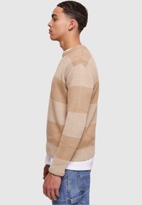 Pulover rayé bej și crem cu guler rotund, mansete cu nervuri și tricot texturat. Purtați peste o cămașă albă, asortat cu blugi.