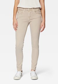 Beige skinny jeans made of denim with a smooth texture, featuring five pockets, a front button closure, and contrasting stitching details.