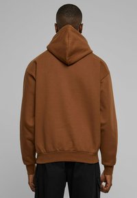 Felpa con cappuccio marrone realizzata in tessuto morbido, con un fit rilassato, polsini e orlo a coste. Design semplice senza loghi o motivi visibili.