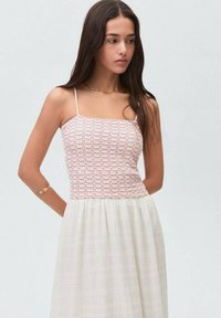 Vit klänning med en smockad bodice i röd mönster och tunna axelband, med en flödande vit kjol med subtil textur och horisontella ränder.