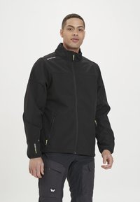 Czarna kurtka typu softshell z wysokim kołnierzem, żółtymi akcentami zamka i dwiema bocznymi kieszeniami. Charakteryzuje się detalami przeszycia, które nadają jej zorganizowany wygląd.