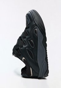 Čierna športová obuv s panelmi zo sieťoviny, textúrovaným koženým zvrškom, polstrovanou podrážkou a šnurovacím dizajnom. Má mierne zvýšený opätok.