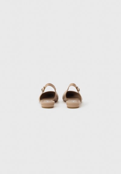 Ζευγάρι μπεζ καφέ παπούτσια με χαμηλό τακούνι και λουράκι στον αστράγαλο, από πίσω, σε ανοιχτό γκρι φόντο.