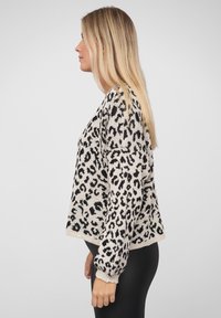 Leopardmønster genser i beige og svart, med en avslappet passform, ribbestrikkede mansjetter og en myk tekstur. Elegant, moderne design.