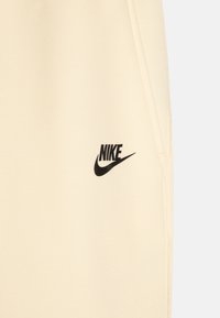 Beige Nike-tröja med svart logotyp. Tillverkad av mjukt tyg, med minimalistisk design och ren sömnad längs kanterna.