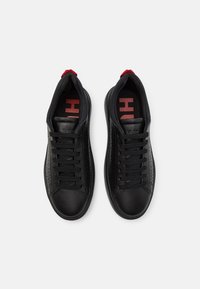 Černé tenisky vyrobené z hladké ků�že s texturovanými bočními panely, kulatou špičkou, černými tkaničkami a červenými akcenty na patě a ve vycpávce.